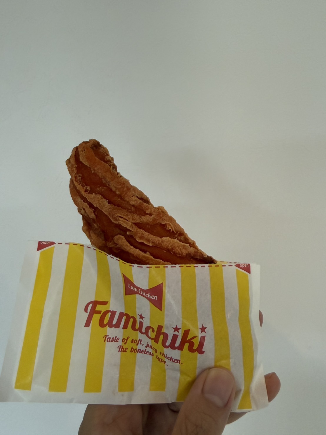 ファミリーマートのクリスピーチキン麻辣湯味を、黄色いストライプ柄のファミチキ用パッケージから取り出して手に持っているところ