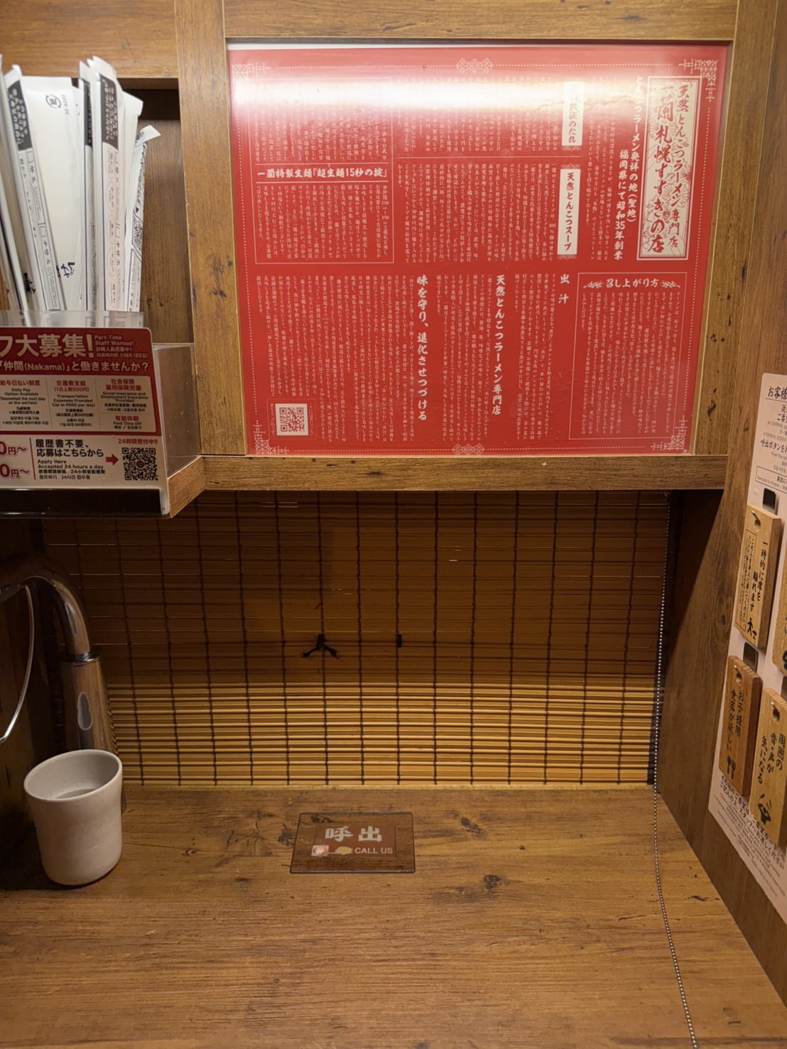 一蘭の個室カウンター席。木の仕切りとのれん、赤い説明書きが見える。呼出ボタンが置いてある