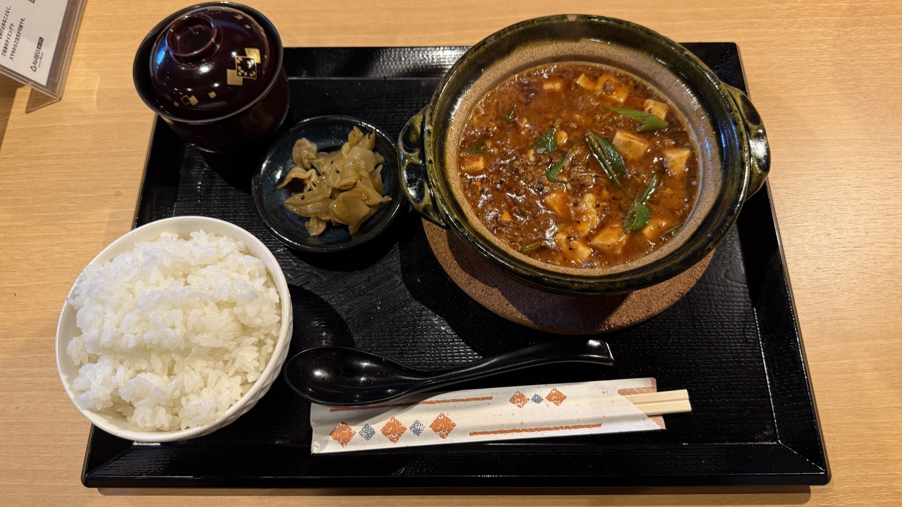 円山麻婆飯店の土鍋麻婆定食。黒い角トレーに、土鍋でぐつぐつ煮込まれた広東麻婆豆腐（赤茶色のスープにとろみがあり花椒の粒が見える）、白いご飯、漬物の小鉢、味噌汁。本格中華の麻婆豆腐がそのままの土鍋で提供される