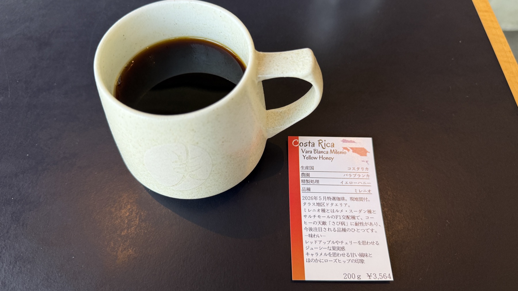 丸美珈琲店のコーヒー。クリーム色のロゴ入りマグカップに浅煎りのコーヒー。横に置かれた説明カードには「Costa Rica - Vara Blanca Milenio Yellow Honey」と書かれている