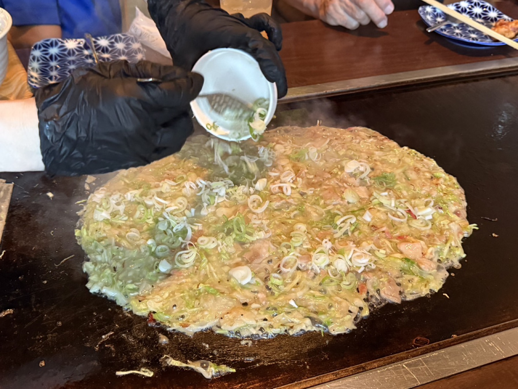 鉄板の上で焼かれる豚ネギ塩もんじゃ。刻んだねぎがたっぷりかけられ、湯気が立っている