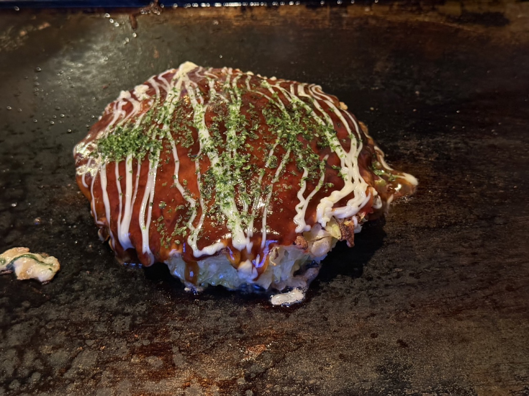 もんじゃ鉄板焼き mill maruyamaのお好み焼き。ソースとマヨネーズが格子状にかけられ、青のりが散らされている