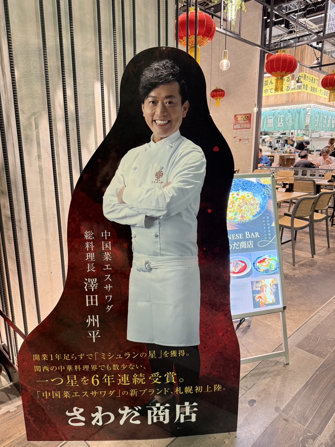 さわだ商店の店頭に置かれた澤田州平シェフの等身大パネル。ミシュランの星を6年連続受賞した経歴が紹介されている