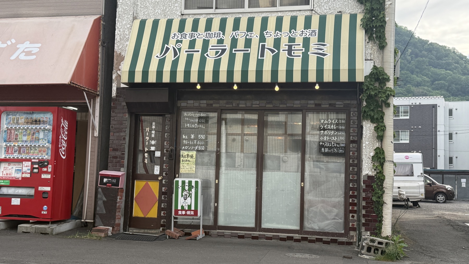 パーラートモミの外観。グリーンと白のストライプの庇に「パーラートモミ」の文字。山を背景に、落ち着いた雰囲気の店構え