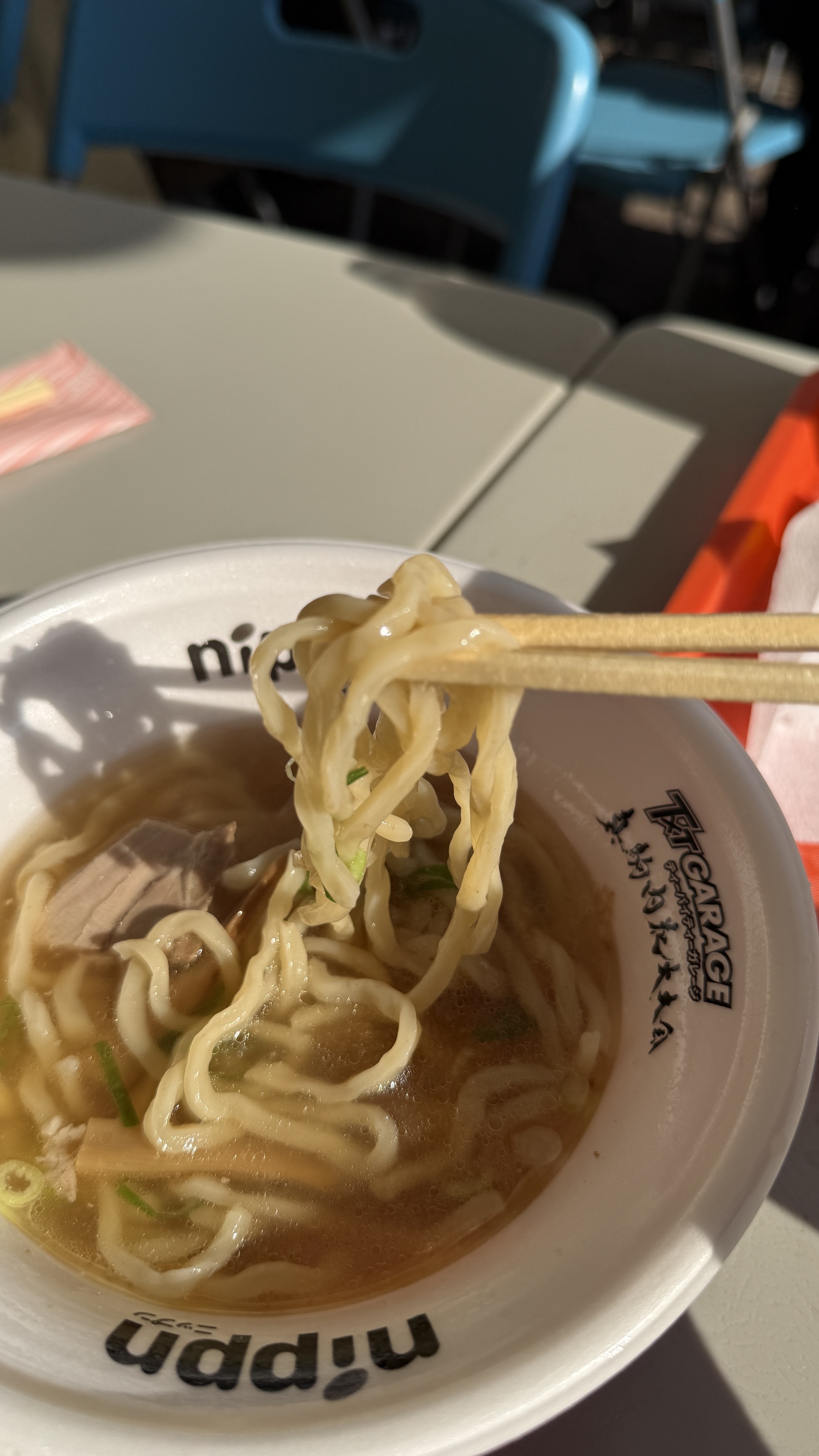 塩ラーメンの麺を箸で持ち上げているところ。黄色いちぢれ麺がたっぷりスープを纏って光っている